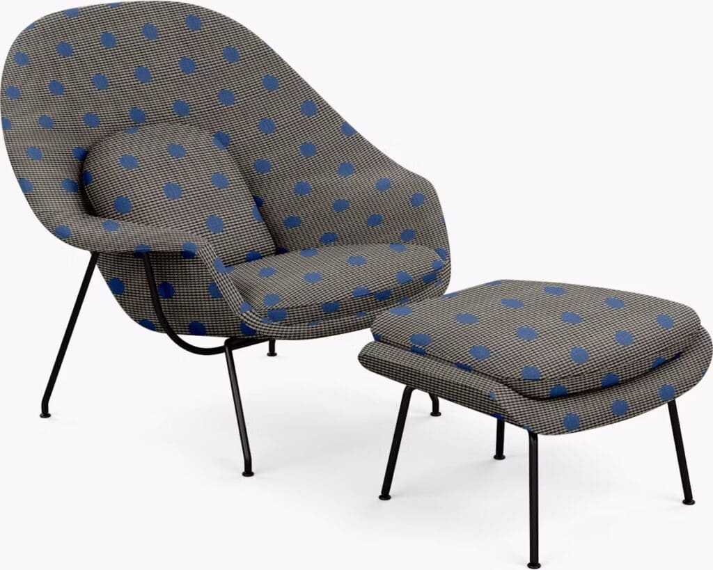 A modern armchair with a rounded backrest and a matching ottoman, both upholstered in a polka dot fabric featuring blue dots on a textured gray background.