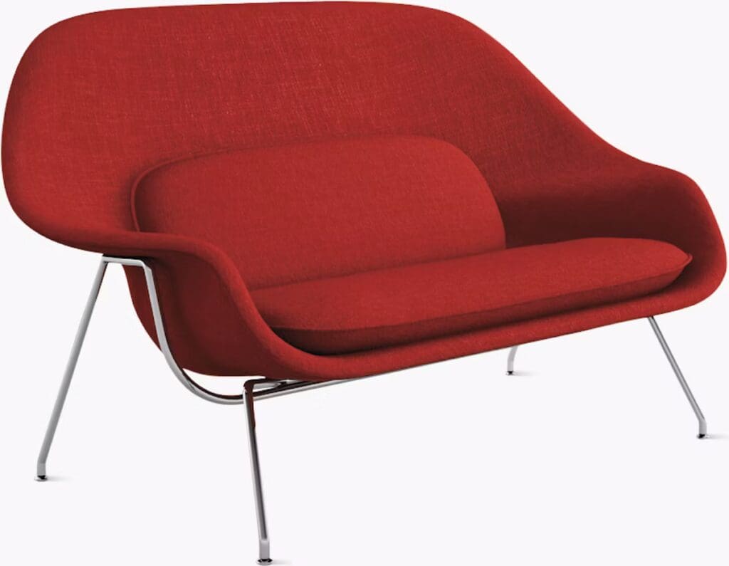 A modern red loveseat with a curved design and chrome legs, designed by Eero Saarinen.