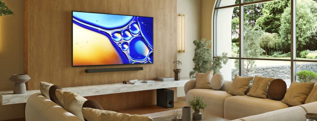 A modern living room with a stylish TV mounted on a wooden wall, featuring light-colored sofas and decorative plants, with large windows showcasing an outdoor view.