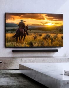 A person on horseback watching a sunset displayed on a mounted television set in a modern living room with minimalist decor.
